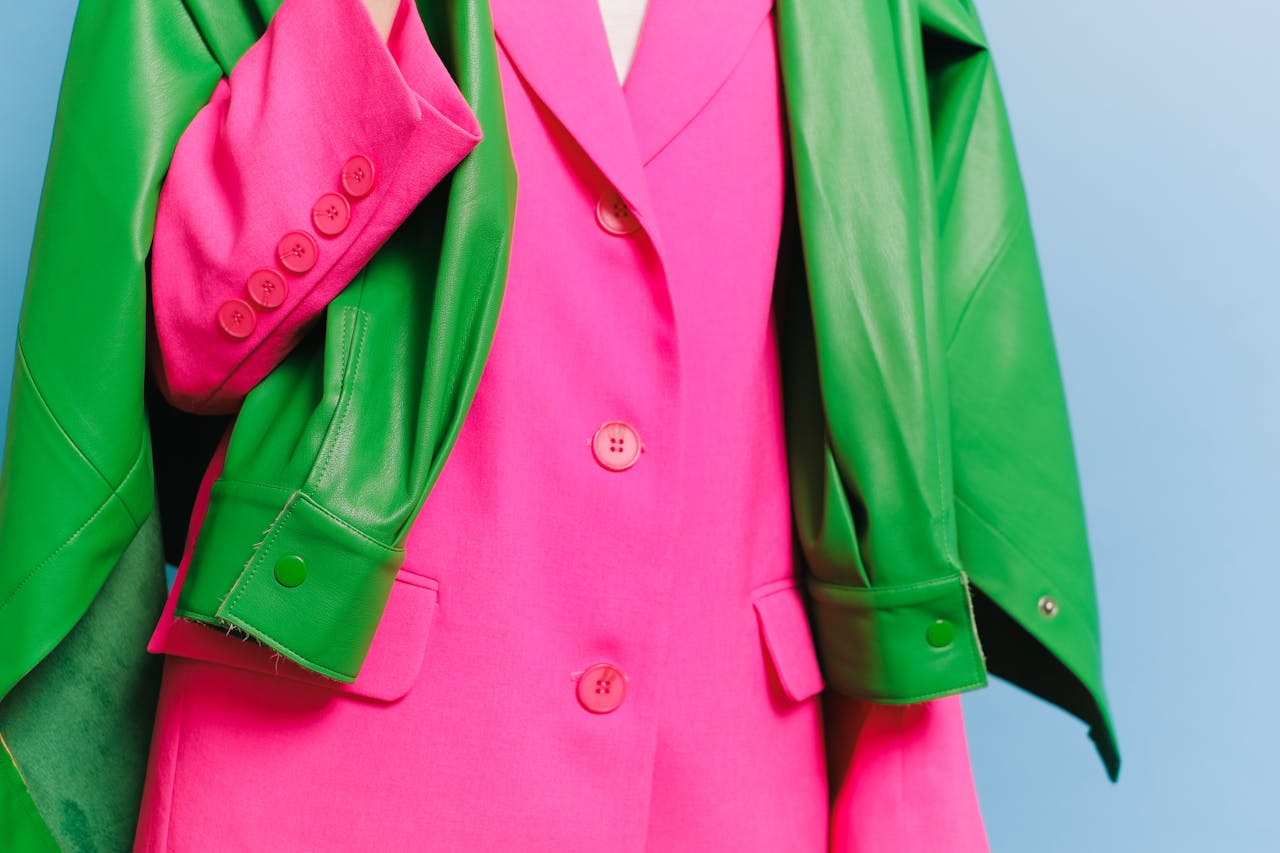 About Stylish pink blazer with a contrasting green leather jacket draped over it, showcasing bold fashion colors.